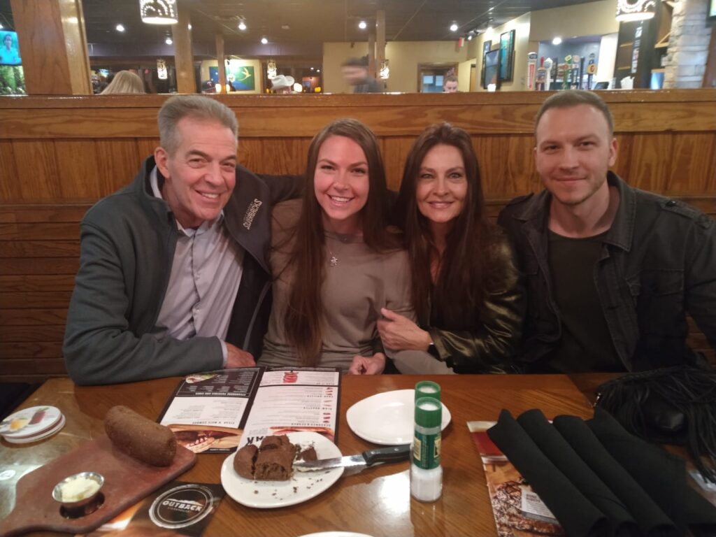 Teige with parents and brother seated at a restaurant table in America