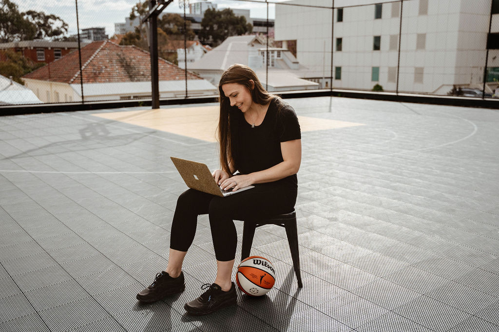 girl typing on laptop while sitting in chair placed on basketball court